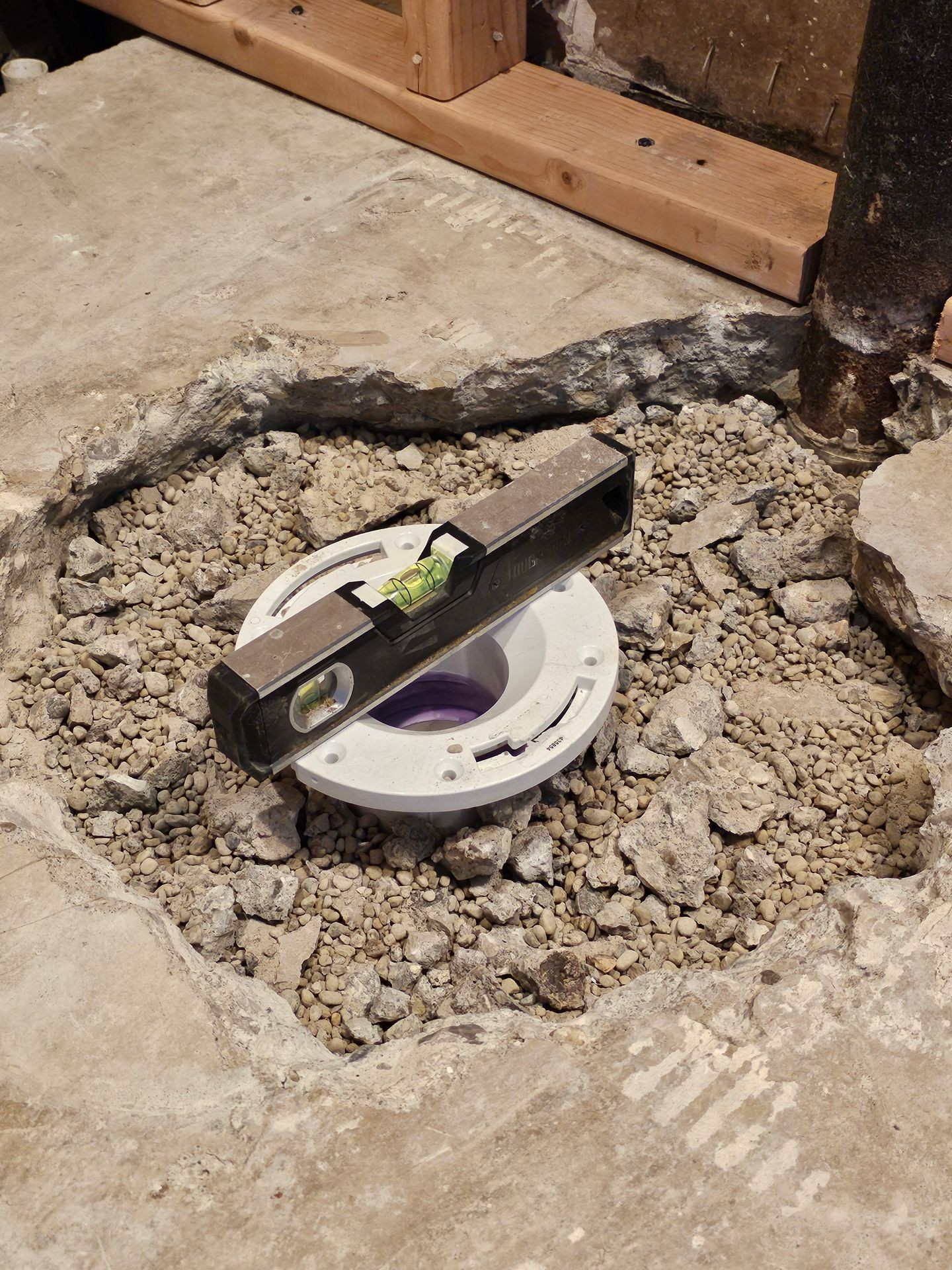 Level tool placed on a toilet flange in a construction site with gravel and floor space around.