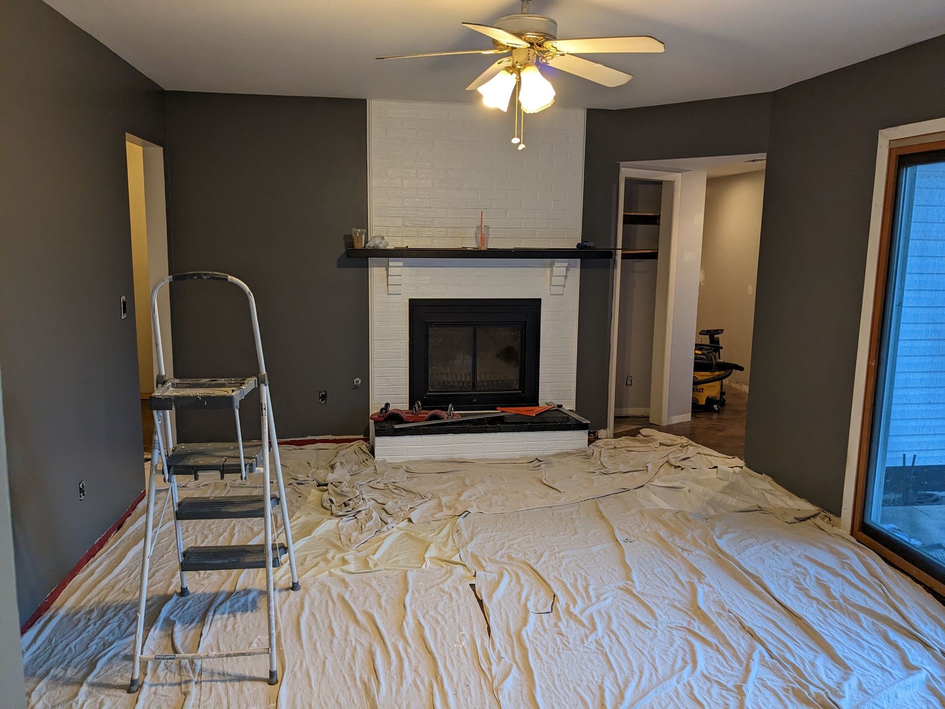 Room under renovation with a ladder, drop cloths, and a fireplace against dark walls.
