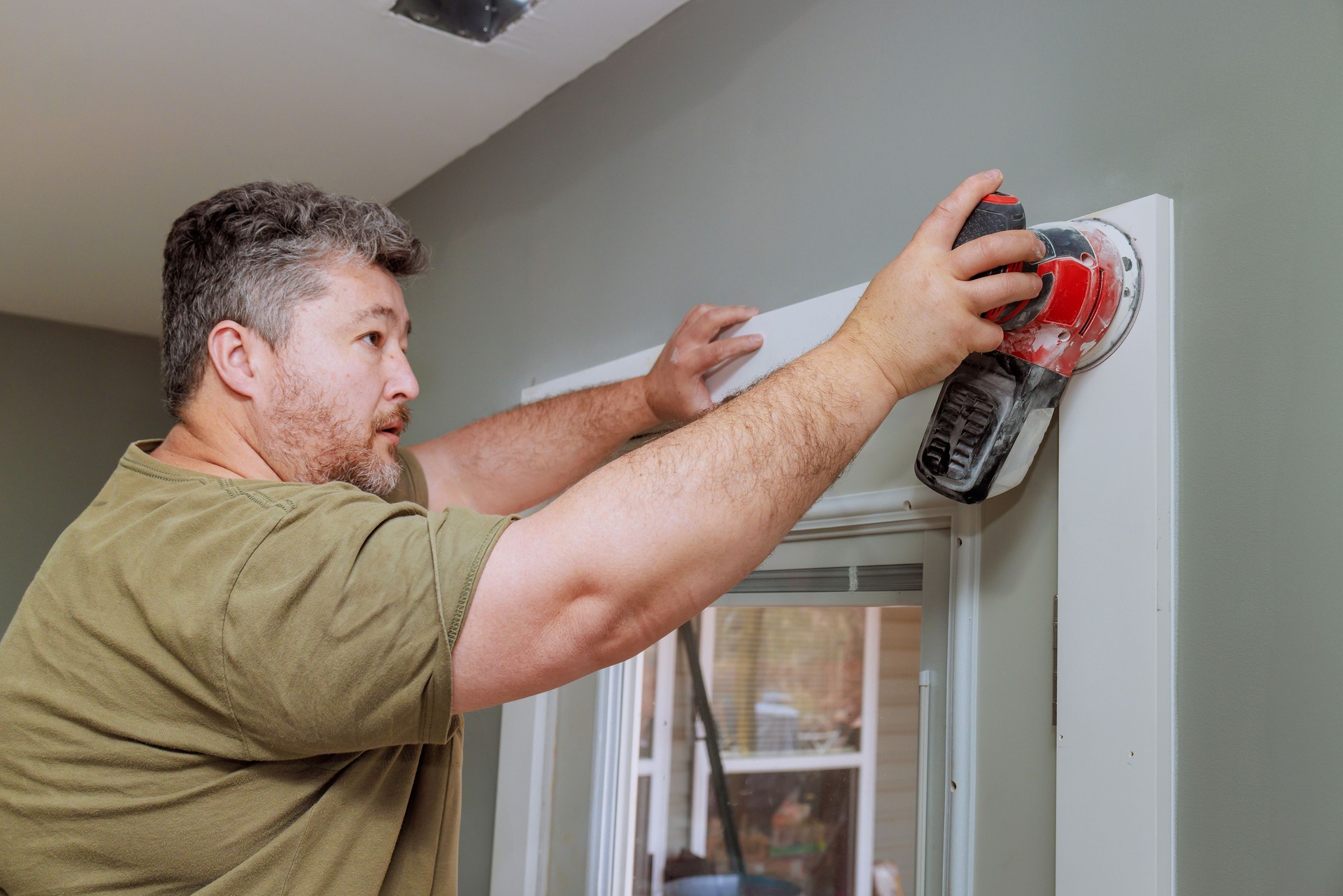 Home improvement project in progress as a man sands the doorway trim during a renovation